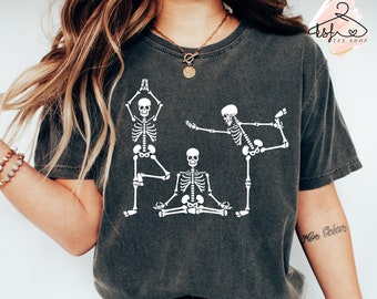 May include: A dark gray t-shirt with a white graphic of three skeletons doing yoga poses. The text "Non Obéir" is written on the right sleeve of the shirt.
