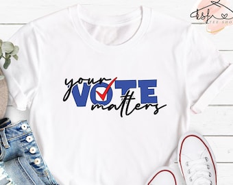 May include: White t-shirt with a blue and red graphic that says "your VOTE matters". The shirt is paired with blue jeans and white sneakers.