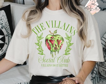 Op de afbeelding: Wit T-shirt met een groene en rode appel afbeelding en de tekst "The Villains Social Club Villains Do It Better".