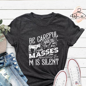 May include: A dark gray t-shirt with a white graphic that says "Be careful when you follow the masses, sometimes the M is silent". The graphic also includes a cartoon donkey.
