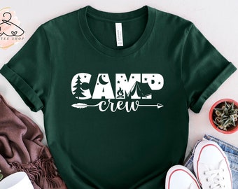 May include: A dark green t-shirt with a white graphic design that says "Camp Crew" with a stylized campfire, tent, and arrow.