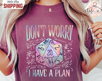Puede incluir: Una camiseta morada con el texto "No te preocupes, tengo un plan" y un dado de 20 caras de color arcoíris rodeado de fórmulas matemáticas.