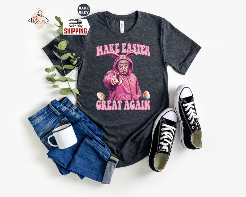 May include: A dark grey t-shirt with a pink bunny rabbit wearing a pink hat and holding an Easter egg. The text "Make Easter Great Again" is printed on the shirt.