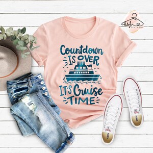 May include: Pink t-shirt with a blue cruise ship graphic and the text "Countdown is over, It's Cruise Time".