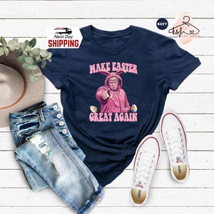 May include: A navy blue t-shirt with a graphic of a person wearing a pink bunny costume and the text "Make Easter Great Again".