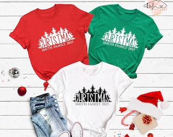 Peut inclure: Trois t-shirts sur le thème de Noël dans les couleurs blanc, rouge et vert. Les t-shirts présentent une silhouette noire d'une forêt avec le texte "Christmas Smith Family 2025".