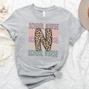 May include: A grey t-shirt with the text "SCHOOL NURSE" repeated in different colours. The letter "N" is a large, leopard print design.