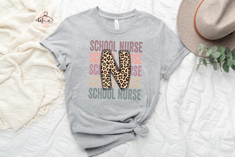 May include: A grey t-shirt with the text "SCHOOL NURSE" repeated in different colours. The letter "N" is a large, leopard print design.
