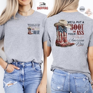 May include: A heather gray t-shirt featuring a graphic of cowboy boots with the American flag design and a cowboy hat. The text on the back reads "We'll put a boot in your ass the American way."