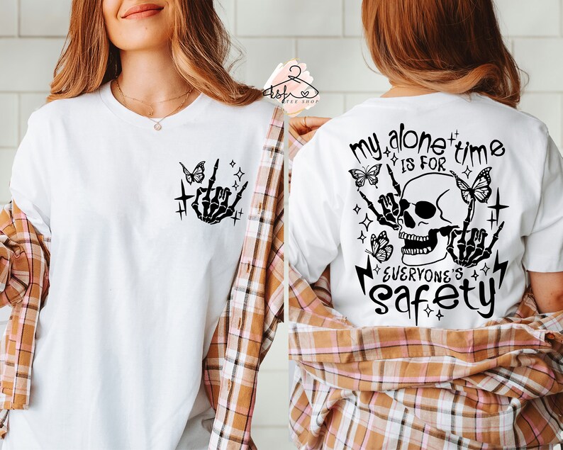 Puede incluir: Camiseta blanca con un dise&ntilde;o negro de calavera y huesos cruzados. La calavera tiene una sonrisa diab&oacute;lica y est&aacute; rodeada de mariposas y estrellas. El texto "My alone time is for everyone's safety" est&aacute; impreso debajo de la calavera.