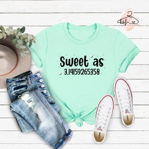 May include: A light blue t-shirt with the text "Sweet as 3,14159265358" in black. The text is surrounded by small white stars and hearts.