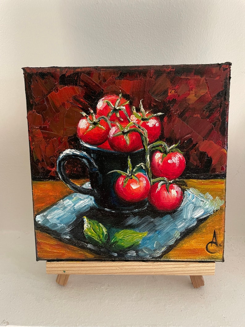 May include: A painting of a still life featuring a black ceramic mug filled with red tomatoes on a vine. The mug is sitting on a blue and white patterned napkin on a wooden surface. The background is a dark red.
