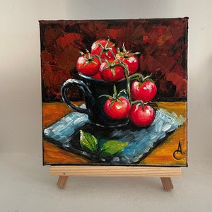 May include: A painting of a black ceramic mug filled with red tomatoes on a vine. The mug is sitting on a blue and brown patterned surface. The background is a dark red.