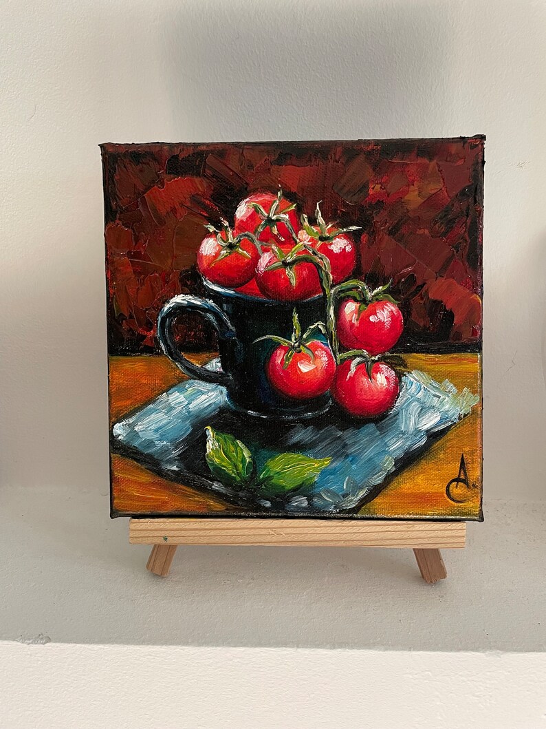 May include: A painting of a black ceramic mug filled with red tomatoes on a vine. The mug is sitting on a blue and brown patterned surface. The background is a dark red.