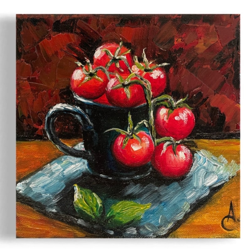 May include: A black ceramic mug filled with red ripe tomatoes on a vine. The mug is sitting on a blue and white patterned napkin on a wooden surface.
