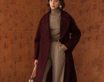 Può includere: Un lungo cappotto in lana color bordeaux scuro indossato sopra un maglione a collo alto beige e pantaloni beige abbinati a gamba larga. L'outfit include una cintura in pelle marrone, una borsa strutturata beige e décolleté con stampa pitonata.