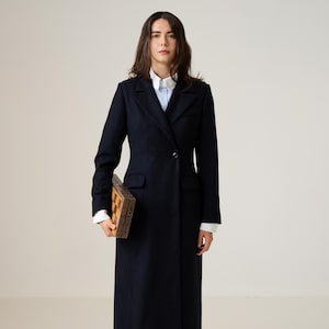 May include: A long, navy blue coat with a single button closure. The coat is worn over a white collared shirt and dark pants. A wooden chessboard is held in the person's hands.