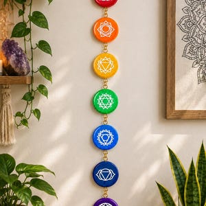 Peut inclure: Une décoration murale verticale composée de sept disques circulaires aux couleurs de l'arc-en-ciel, incluant le rouge, l'orange, le jaune, le vert, le bleu, l'indigo et le violet. Chaque disque présente un symbole géométrique blanc unique.
