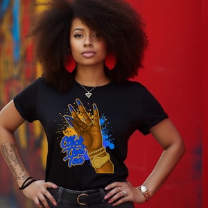 May include: Black t-shirt with a graphic of a hand with blue fingernails, a gold watch, and the text "Black That Tea" in blue and yellow. The shirt is worn by a person with curly hair and red earrings.