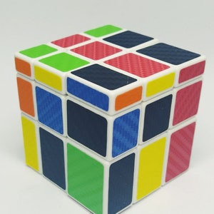 May include: A colorful Rubik's Cube with a white frame and squares in various colors, including red, green, blue, yellow, and orange. The cube has a carbon fiber pattern on the colored squares.