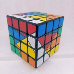 Puede incluir: Un cubo de Rubik 3x3 negro con una variedad de colores, incluyendo rojo, azul, verde, amarillo, naranja y blanco. El cubo está en un estado revuelto.
