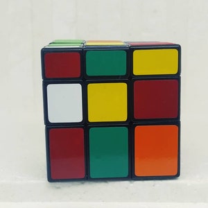 May include: A classic Rubik's Cube with a black frame and colorful squares. The cube features red, green, yellow, white, and orange squares. The puzzle is a 3x3 cube, a popular brain teaser.