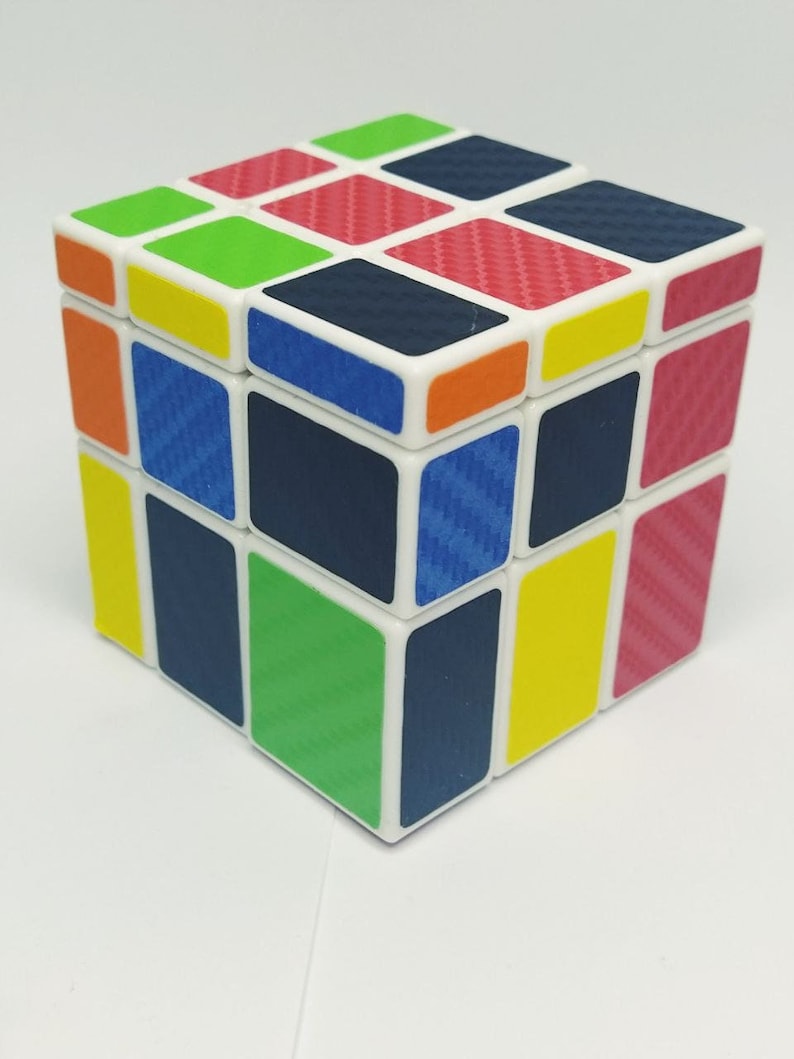 May include: A colorful Rubik's Cube with a white frame and squares in various colors, including red, green, blue, yellow, and orange. The cube has a carbon fiber pattern on the colored squares.