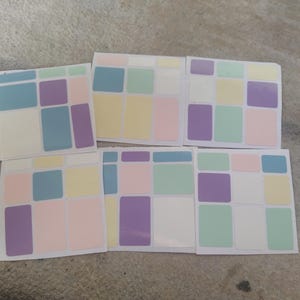 May include: A collection of six square stickers with a pastel color block design. Each sticker features a grid of rectangular shapes in shades of blue, purple, yellow, pink, and green, set against a white background. The stickers are arranged on a neutral surface.