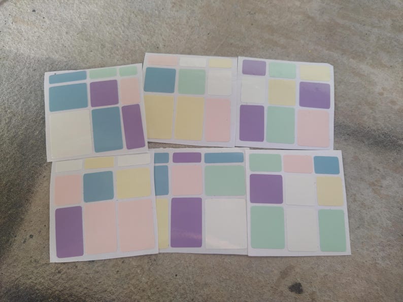 May include: A collection of six square stickers with a pastel color block design. Each sticker features a grid of rectangular shapes in shades of blue, purple, yellow, pink, and green, set against a white background. The stickers are arranged on a neutral surface.