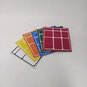Pode incluir: Cinco adesivos quadrados com um padrão de grade. Os adesivos são sobrepostos e são nas cores amarelo, laranja, azul, verde e vermelho.