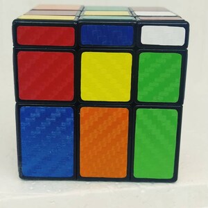 May include: A classic Rubik's Cube puzzle with a black frame and colorful squares. The cube features red, yellow, green, blue, orange, and white sides. The squares have a textured pattern. A popular brain teaser and toy.