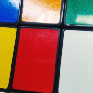 May include: Close-up of a colorful Rubik's Cube with squares in blue, orange, green, yellow, red, and white. The cube's black edges frame each colored square, creating a classic puzzle toy.