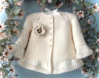 May include: A white knitted baby cardigan with a flower embellishment and button closure.