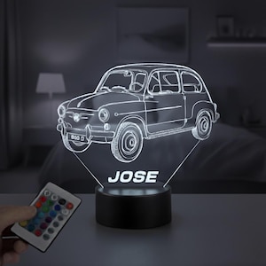 Può includere: Luce notturna a LED 3D con design di un'auto classica. L'auto bianca è illuminata, con il nome "JOSE" visualizzato sulla base. È visibile un telecomando con opzioni di colore.