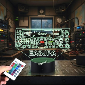Pode incluir: Um design de receptor de rádio com contorno verde é iluminado acima de uma base preta com o texto "EA3JPA". Uma mão segura um controle remoto com várias opções de cores. A base tem o texto "Fragancii".