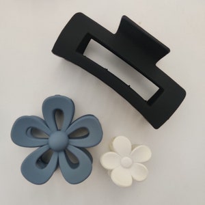 May include: Three hair clips in different shapes and colors. A black rectangle-shaped clip, a blue flower-shaped clip, and a white flower-shaped clip.