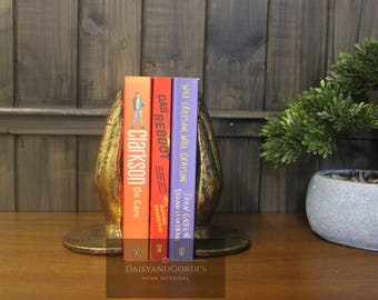 May include: Gold metal bookends in the shape of hands holding up three books. The books are titled "Clarkson on Cars", "Das Reboot", and "Will Grayson, Will Grayson".