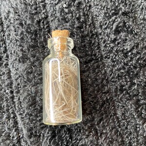 May include: A small glass bottle with a cork stopper filled with light brown hair-like fibers.