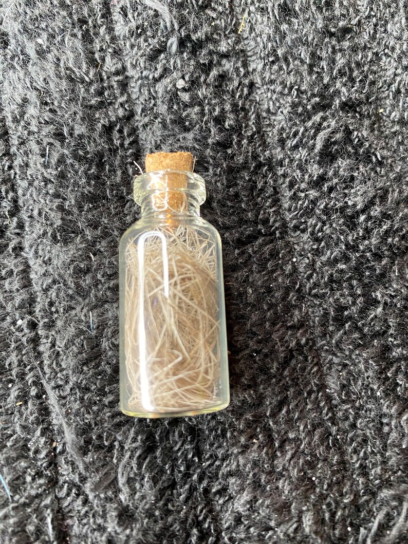 May include: A small glass bottle with a cork stopper filled with light brown hair-like fibers.
