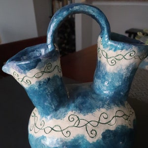 Może przedstawiać: Niebieski ceramiczny wazon z dwoma wylewkami i uchwytem. Wazon jest ozdobiony białymi i zielonymi spiralami.