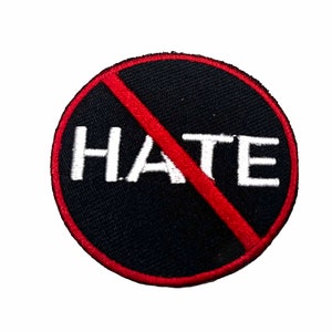 May include: A round patch with a black background and a red border. The word "HATE" is written in white, with a red diagonal line through it. The patch is likely made of fabric.
