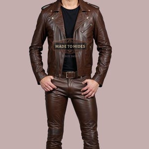 Puede incluir: Una chaqueta de cuero marr&oacute;n con cierre de cremallera y un cintur&oacute;n de cuero marr&oacute;n. La chaqueta tiene un logotipo "MADE TO HIDES" en la parte delantera. La persona lleva pantalones de cuero marr&oacute;n.