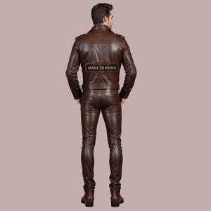 Puede incluir: Una chaqueta de cuero marr&oacute;n y pantalones a juego. La chaqueta tiene cierre de cremallera y cuello alto. Los pantalones tienen un ajuste delgado. El texto "MADE TO HIDES" est&aacute; impreso en la parte posterior de la chaqueta.