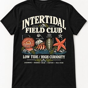 May include: A black t-shirt featuring a graphic print with the text "INTERTIDAL FIELD CLUB" and "LOW TIDE / HIGH CURIOSITY". The design displays illustrations of an anemone, a hermit crab, a chiton, and a sea star, with labels at the bottom.