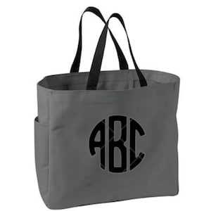 May include: Gray tote bag with black handles and a side pocket. The bag features a large, black monogram with the letters "ABC" in a circular design. The tote is made of a sturdy material.