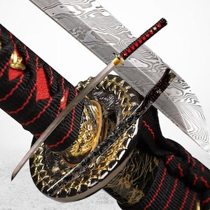 May include: A traditional Japanese katana sword with a black and red scabbard. The sword has a silver blade with a decorative pattern and a red and gold handle.