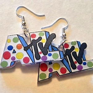 May include: A pair of dangle earrings featuring the letters MTV in a stylized font. The letters are white with colorful polka dots in red, yellow, green, blue, and purple. A large black letter M overlaps the white letters, and silver hooks are attached.