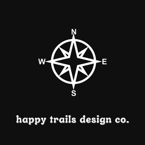 May include: A white compass with the letters N, S, E, and W on a black background. The text "happy trails design co." is below the compass.