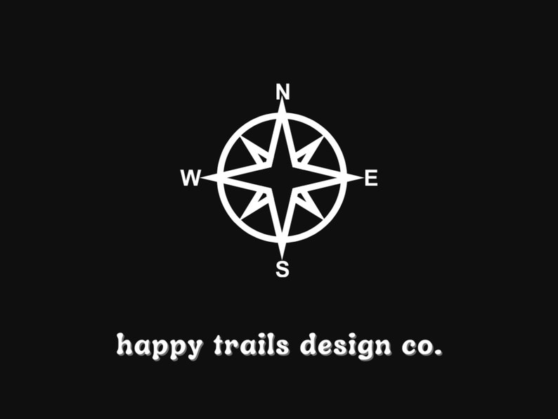 May include: A white compass with the letters N, S, E, and W on a black background. The text "happy trails design co." is below the compass.