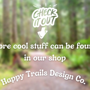 May include: A blurred image of a forest path with the text "CHECK ITOUT" in a white speech bubble with an arrow pointing down. The text "More cool stuff can be found in our shop Happy Trails Design Co." is below the speech bubble.